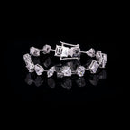 A silver tennis bracelet featuring a mix of round, baguette, and marquise-cut clear stones, displayed on a reflective black surface against a solid black background.